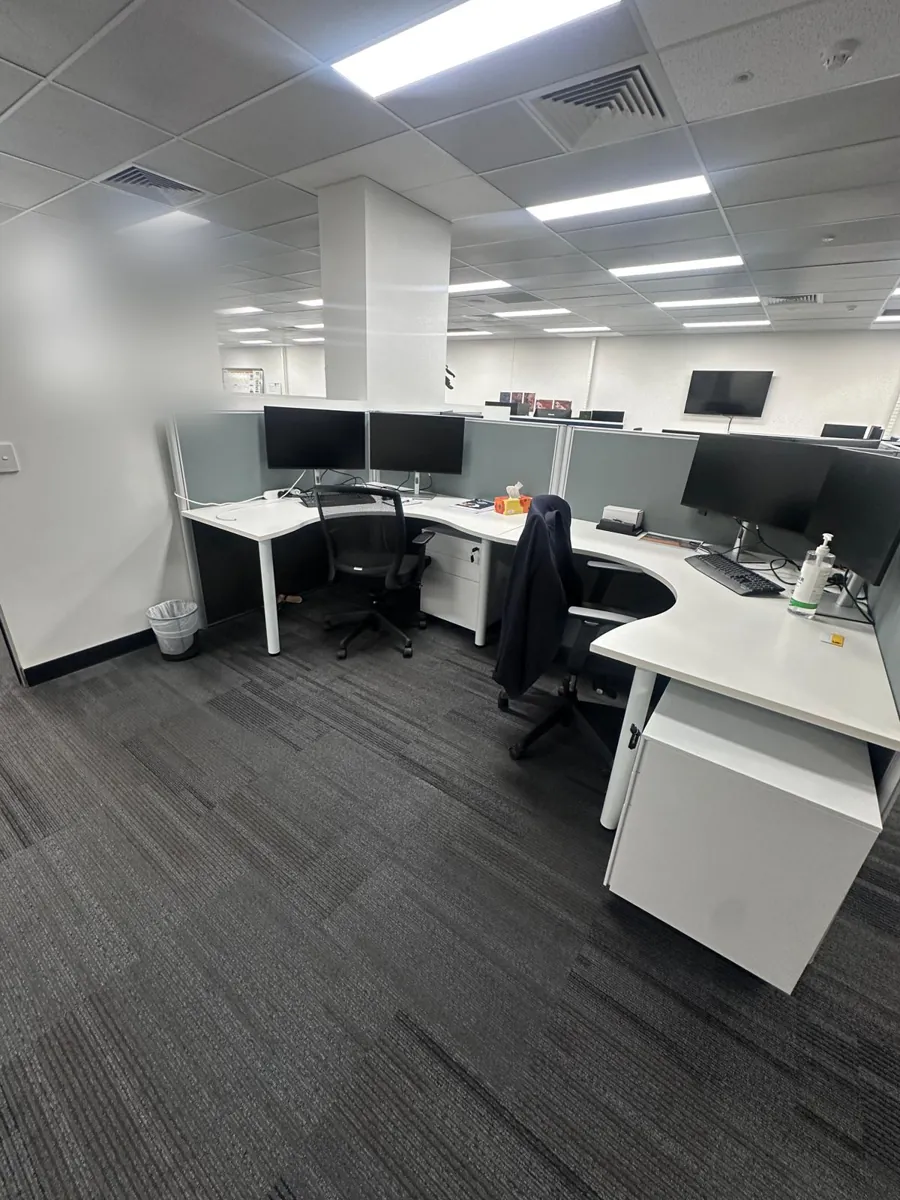 Curved office workstations with dual monitors on dark carpet tiles