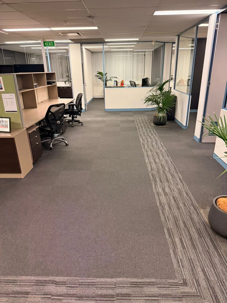 Open plan office with grey carpet tiles, workstations and a reception desk in the distance