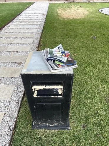Black letterbox overflowing with junk mail on a front lawn