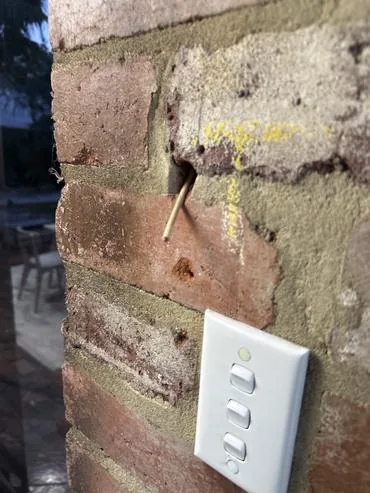 Cable protruding from a brick wall cavity above a light switch