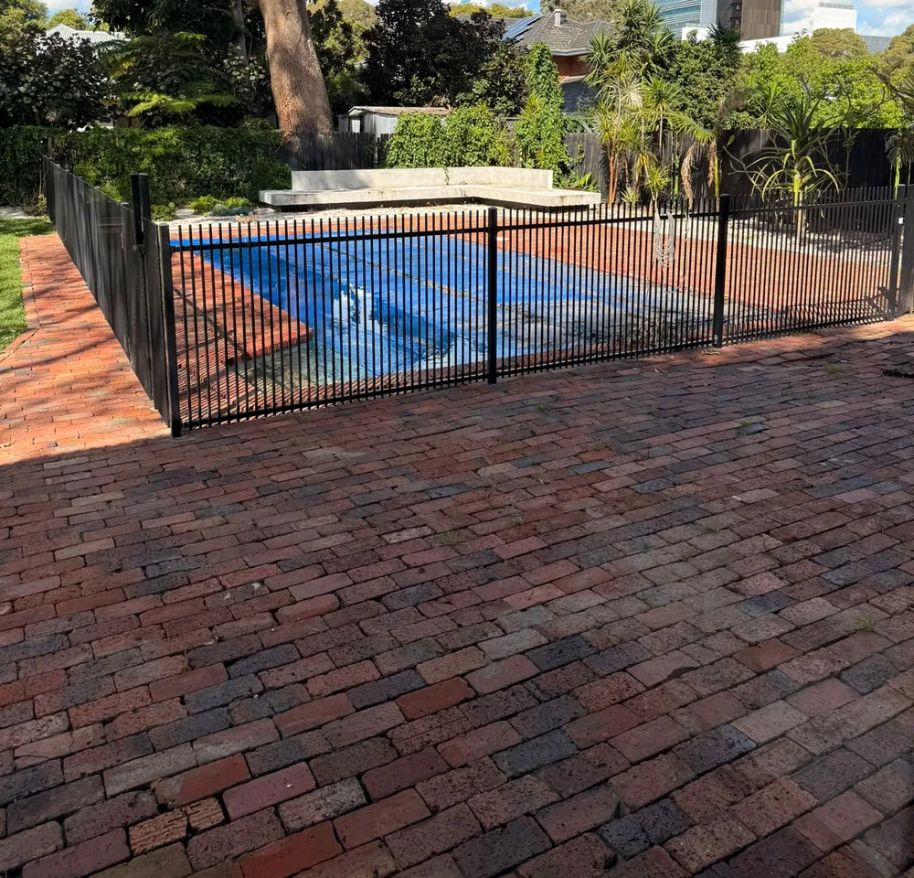 Fenced pool seen across brick paving