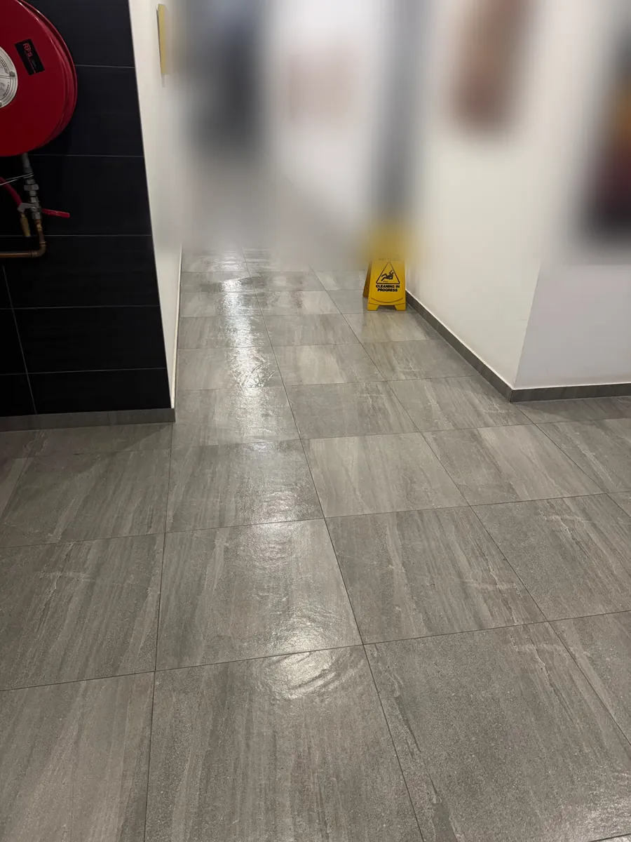 Freshly mopped grey tiled common corridor with a wet floor sign