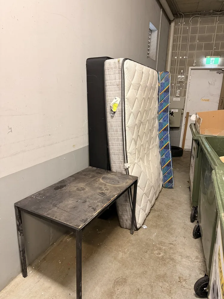 Mattresses, a table and other hard rubbish in a strata building bin area before removal