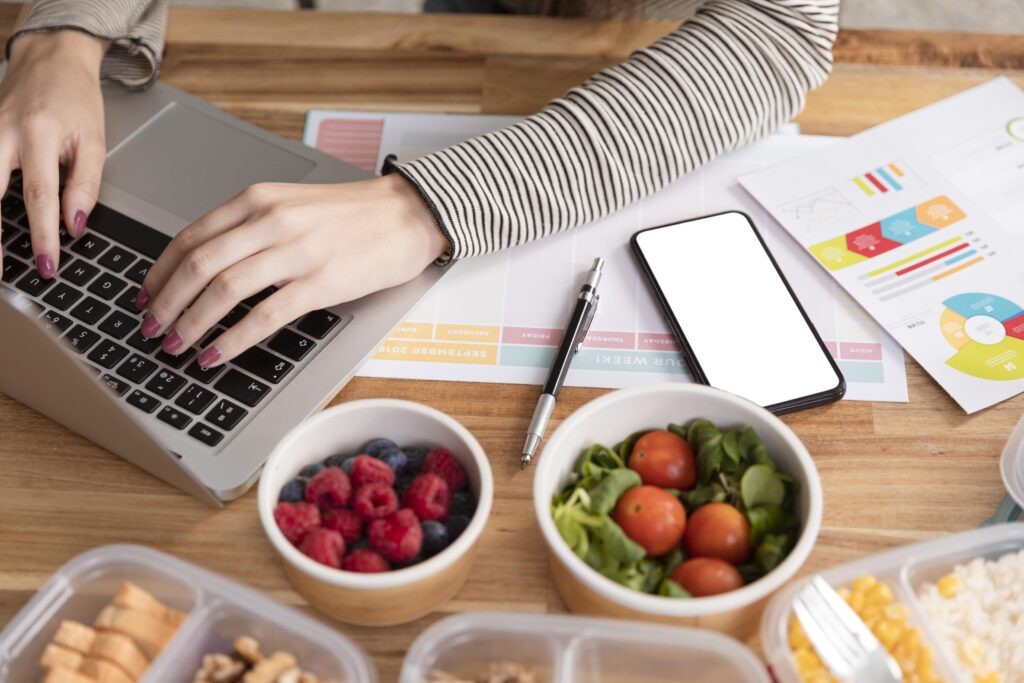 Event planner working at a laptop surrounded by printed schedules and catering checklists, looking focused and slightly stressed.